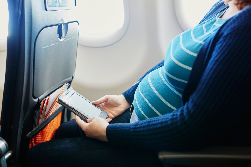 Mulher grávida em voo lendo no assento, viajando com proteção do seguro viagem para gestante